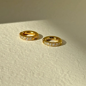 Detail of gold huggie hoop earrings with white zircon stones on textured background