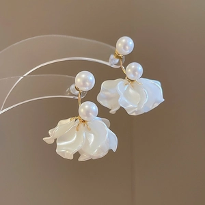 Detailed view of white pearl earrings with gold pins and flower petal accents