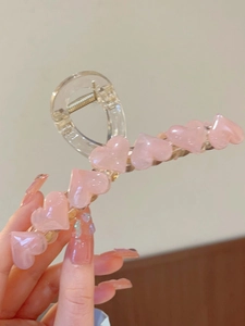 Detail view of a large translucent hair claw clip with multiple pink heart decorations