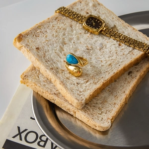 Gold square watch and teardrop turquoise ring set on a creative bread display