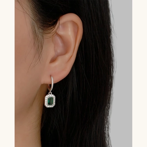 Macro shot of silver emerald green rectangle earring with diamond halo on ear