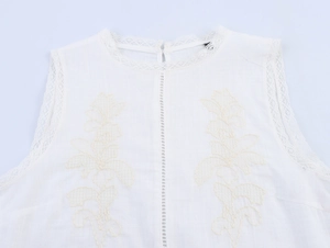Detail of white sleeveless top with delicate lace trim and yellow floral embroidery