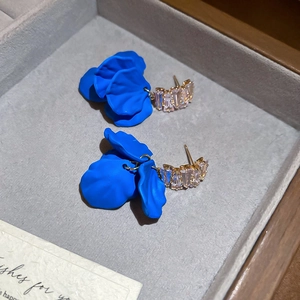 Macro detail of blue frosted petal earrings with gold base and zircon stones on grey velvet