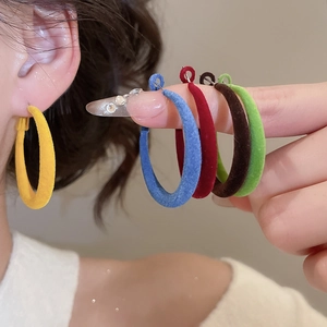 Gros plan de créoles en velours en forme de C en plusieurs couleurs portées par un mannequin