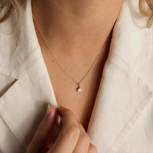 Elegant gold chain necklace with round sparkling stone pendant worn by model