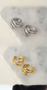 Close-up of triple-layered geometric gold and silver ear clips on marble stone background