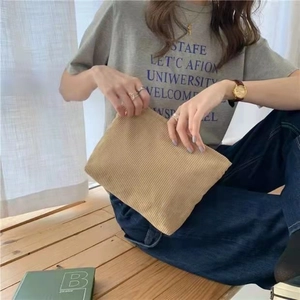 Minimalist beige corduroy clutch bag with ribbed texture shown in hand by a model