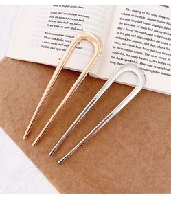 Detail of gold and silver U-shaped metal hair pins on kraft paper with book background
