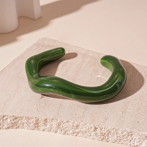 Detail of green marbled acrylic open bangle showing wave texture on a stone slab