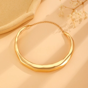 Close-up of golden wavy liquid metal choker necklace with extension chain on beige surface