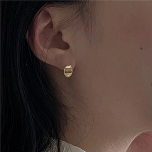 Close-up of elegant gold oval textured earrings worn by a model in a minimalist style