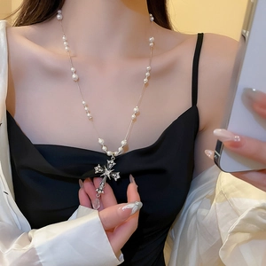 Dettaglio della collana con pendente a croce con strass e perle sul collo femminile