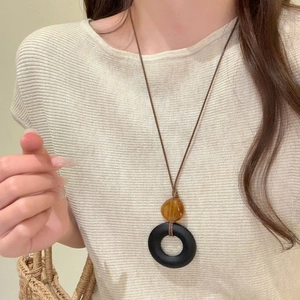 Close-up of resin amber bead and black donut pendant necklace on brown wax cord