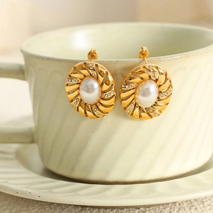 Boucle d'oreille rétro dorée avec perle et strass posée sur une tasse à café