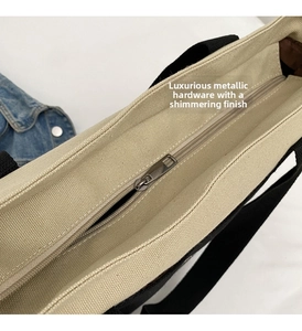 Detail view of canvas tote bag featuring silver metal zipper and black webbing handle