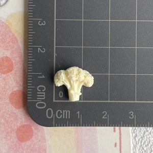 Nahaufnahme einer 1,5 cm Miniatur-Brokkoli-Figur aus Harz auf einer Messskala