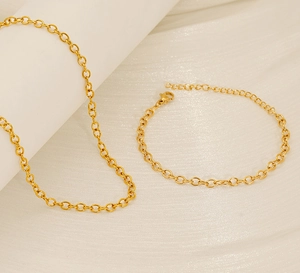 Close-up of golden O-chain necklace and bracelet set on minimalist texture fabric