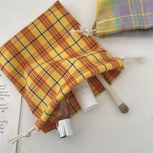 Close-up of a yellow and orange plaid drawstring storage pouch holding cosmetics