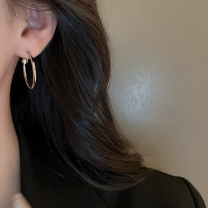 Close-up of a minimalist silver geometric hoop earring worn by a model in soft lighting