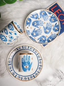 Artistic layout of blue and gold Hamsa hand ceramic cups and plates on white fur background