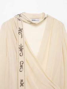 Close-up of beige chiffon blouse with intricate silver sequin beadwork and neck tie detail
