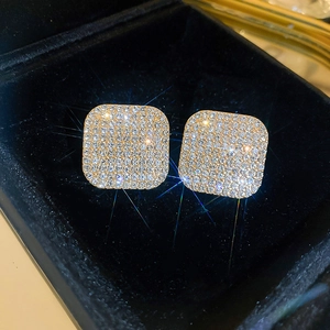 Macro shot of gold square stud earrings with clear sparkling pavé zircons on black velvet