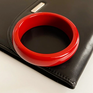 Bracelet jonc en résine rouge poli présenté sur une surface en cuir noir texturé