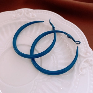 Close-up of deep blue glossy hoop earrings placed on a white decorative porcelain plate