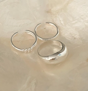 Detailed view of 925 silver knotted and wide band rings set on a textured marble background