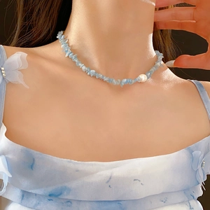 Detail showing irregular light blue aquamarine stones and a pearl necklace on a model