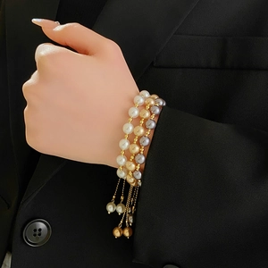 Close-up of triple-layered pearl bracelet with adjustable gold-tone drawstring and beads