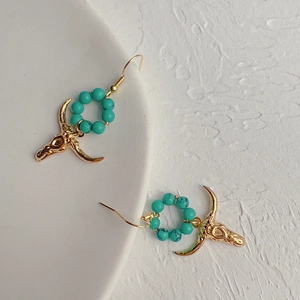 Close-up of golden bull head earrings with turquoise beads on a textured background