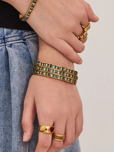 Detail of stacked gold plated bangles with colorful zircons and heart ring on finger