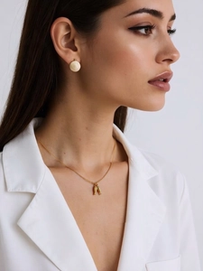Close-up of a model wearing a gold sea-themed fish pendant necklace and matching round studs