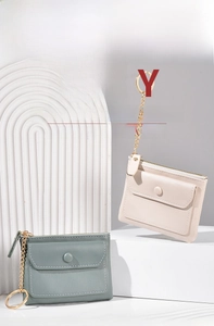 Macro view of beige and green PU leather coin purses with gold hardware on white props
