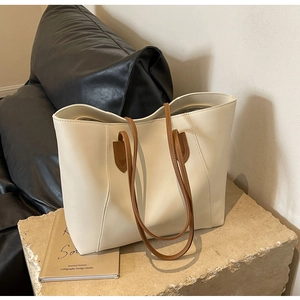 Minimalist cream tote bag with brown straps displayed on a stone platform in detail