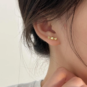 Macro detail of minimalist gold candy-shaped stud earrings worn on a person's ear