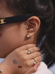 Detail view of pearl earrings and ring with green crown motifs on a model's ear and hand