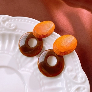 Detail of geometric resin drop earrings with brown wood-texture accents on ceramic plate