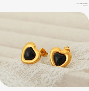 Macro view of gold-plated heart stud earrings with black resin inlay and lace background