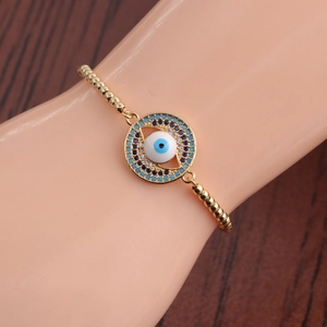 Detail of gold beaded bracelet featuring a blue evil eye pendant on wooden background