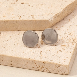 Macro detail of matte silver disc earrings with hand-forged texture on stone background
