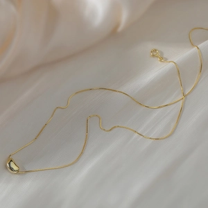 Détail d'un collier chaîne boîte doré avec pendentif haricot sur un fond en soie douce