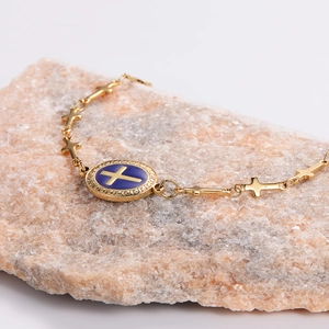 Golden stainless steel cross bracelet with blue oval charm on natural stone background