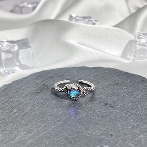 Detail of snake shaped silver ring with blue gemstone on slate and white silk background