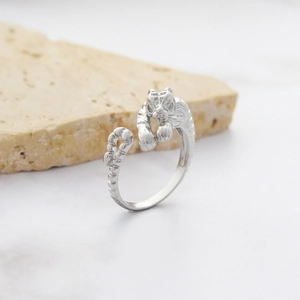 Adjustable silver tiger head ring with polished 18K gold finish on white marble
