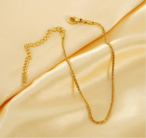 Detailed close-up of gold titanium steel anklet with lobster clasp on silk background