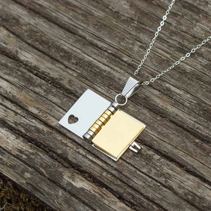 Minimalist stainless steel book locket necklace in gold and silver on a wooden background