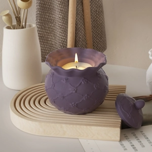 Dettaglio di candela in ceramica viola con rilievi e coperchio su vassoio di legno