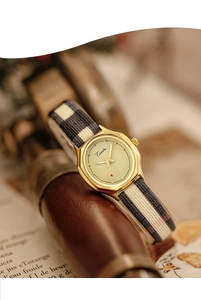 Close-up of vintage oval watch with cream dial and tricolor plaid strap on a rustic book